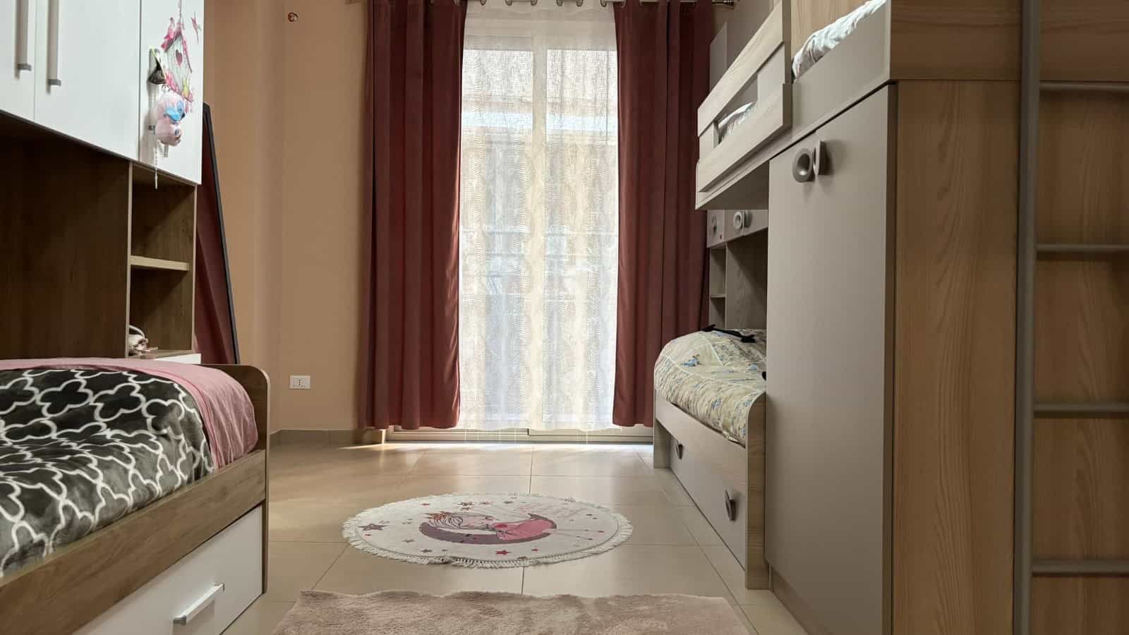 Interno di un appartamento in vendita a Milazzo con letti a castello e grandi finestre con tende rosse.