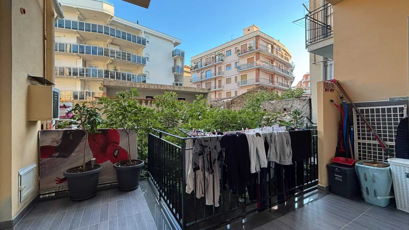 Balcone di un appartamento a Milazzo con piante, stendibiancheria e vista su edifici residenziali moderni.