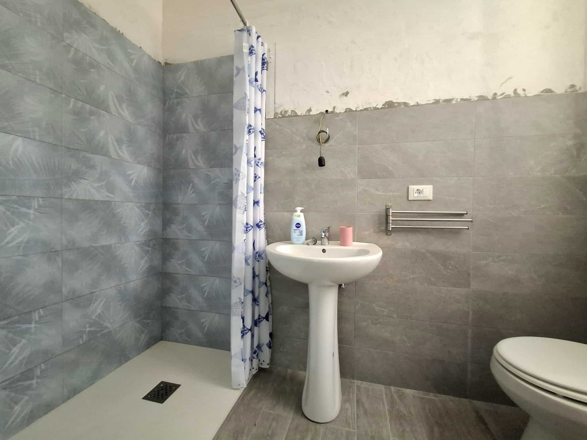 Bagno con piastrelle grigie, lavabo e doccia con tenda, in una casa in vendita a Barcellona P.G.