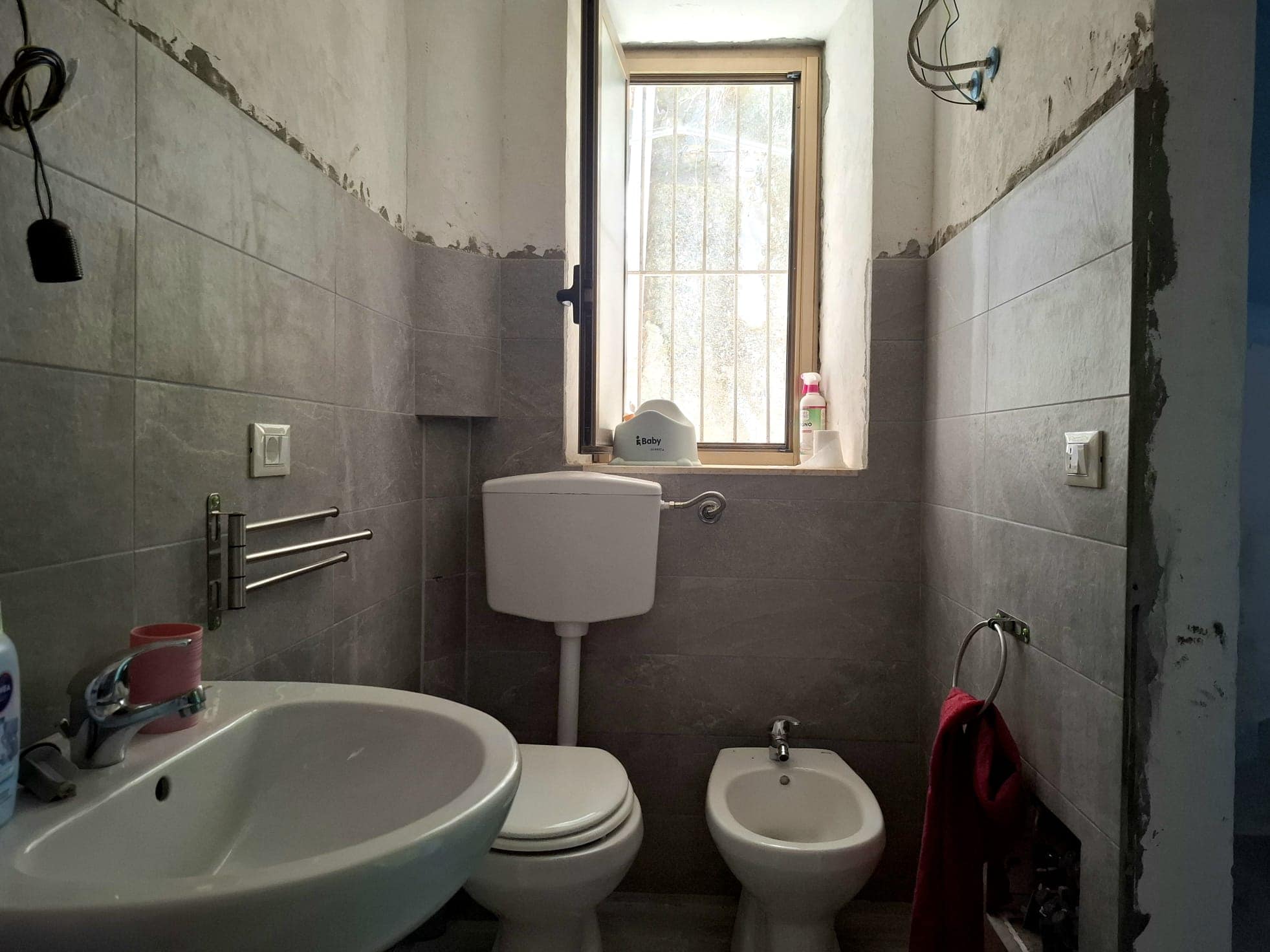 Bagno in fase di ristrutturazione con pareti in piastrelle grigie e finestra.