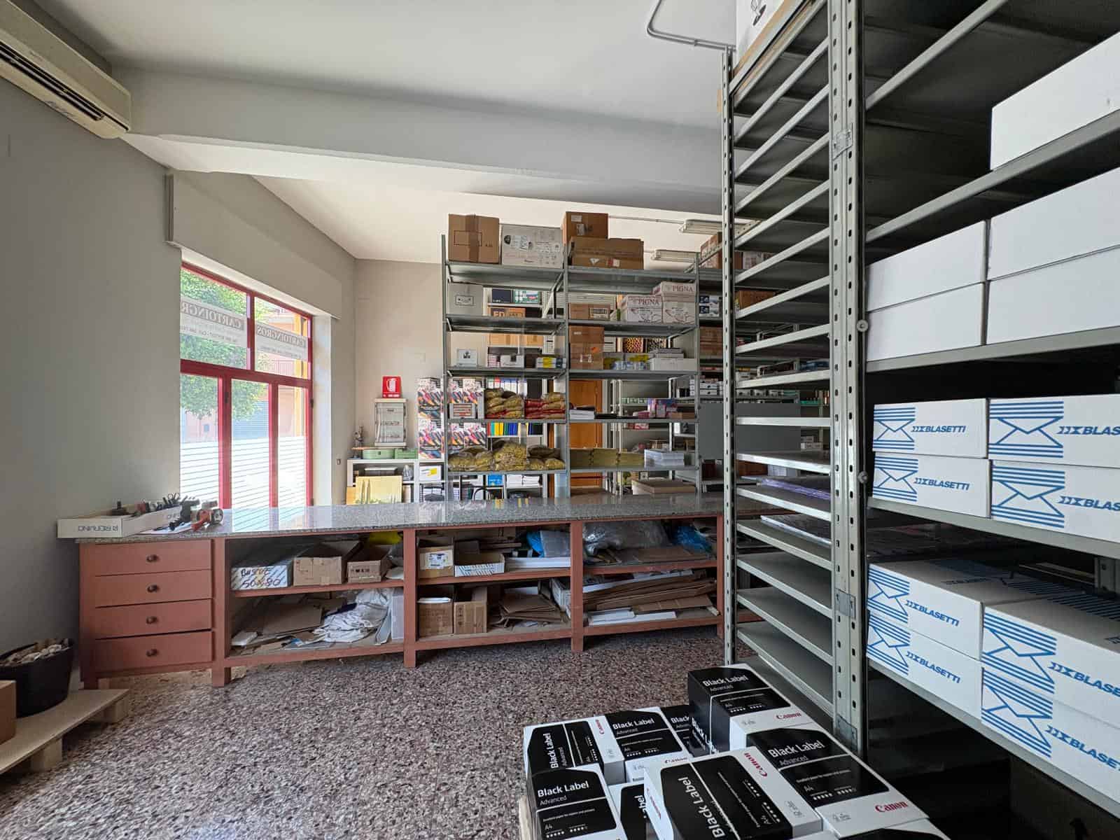 Interno di un magazzino commerciale con scaffalature piene di scatole e materiali vari, illuminato dalla luce naturale.