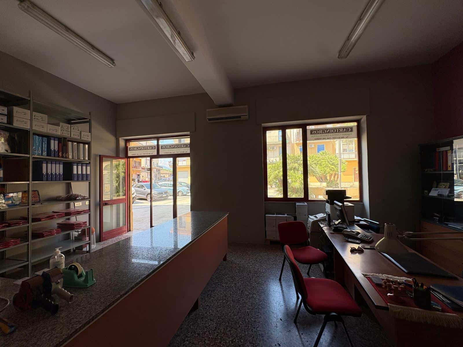 Interno di un ufficio commerciale in affitto a Barcellona P.G. con scrivanie, sedie e scaffali con documenti.