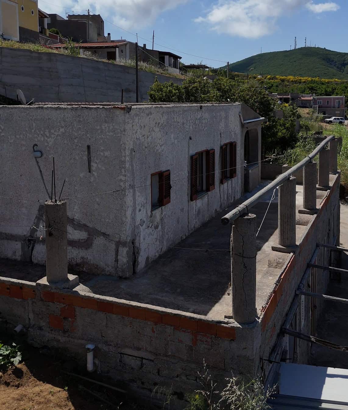 Casa in vendita a Quattropani, Lipari, con pareti in cemento e finestre in legno, vista su colline verdi e cielo sereno.