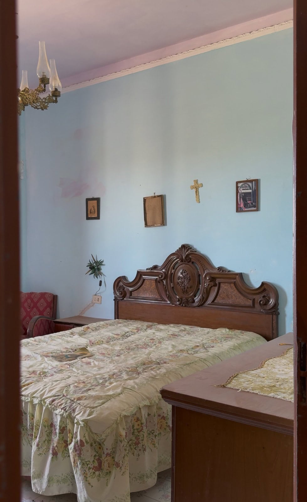 Camera da letto in stile classico con letto in legno intagliato e pareti azzurre, decorata con quadri e croce, in una villa a Lipari.