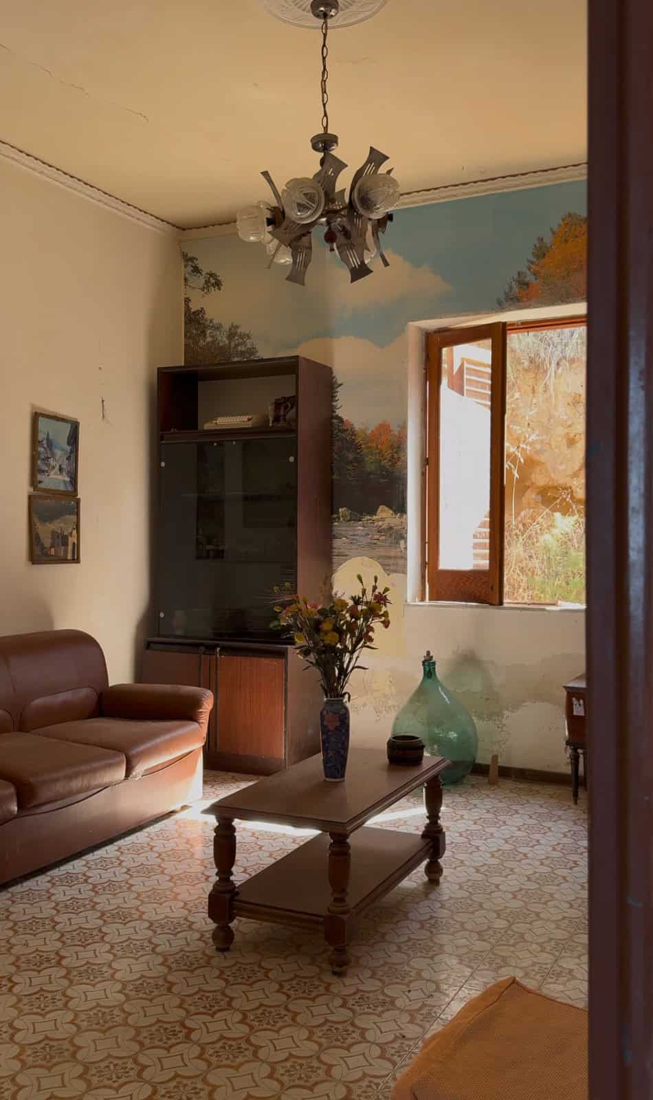 Interno di una casa con divano in pelle, tavolino, e finestra che mostra un paesaggio autunnale.