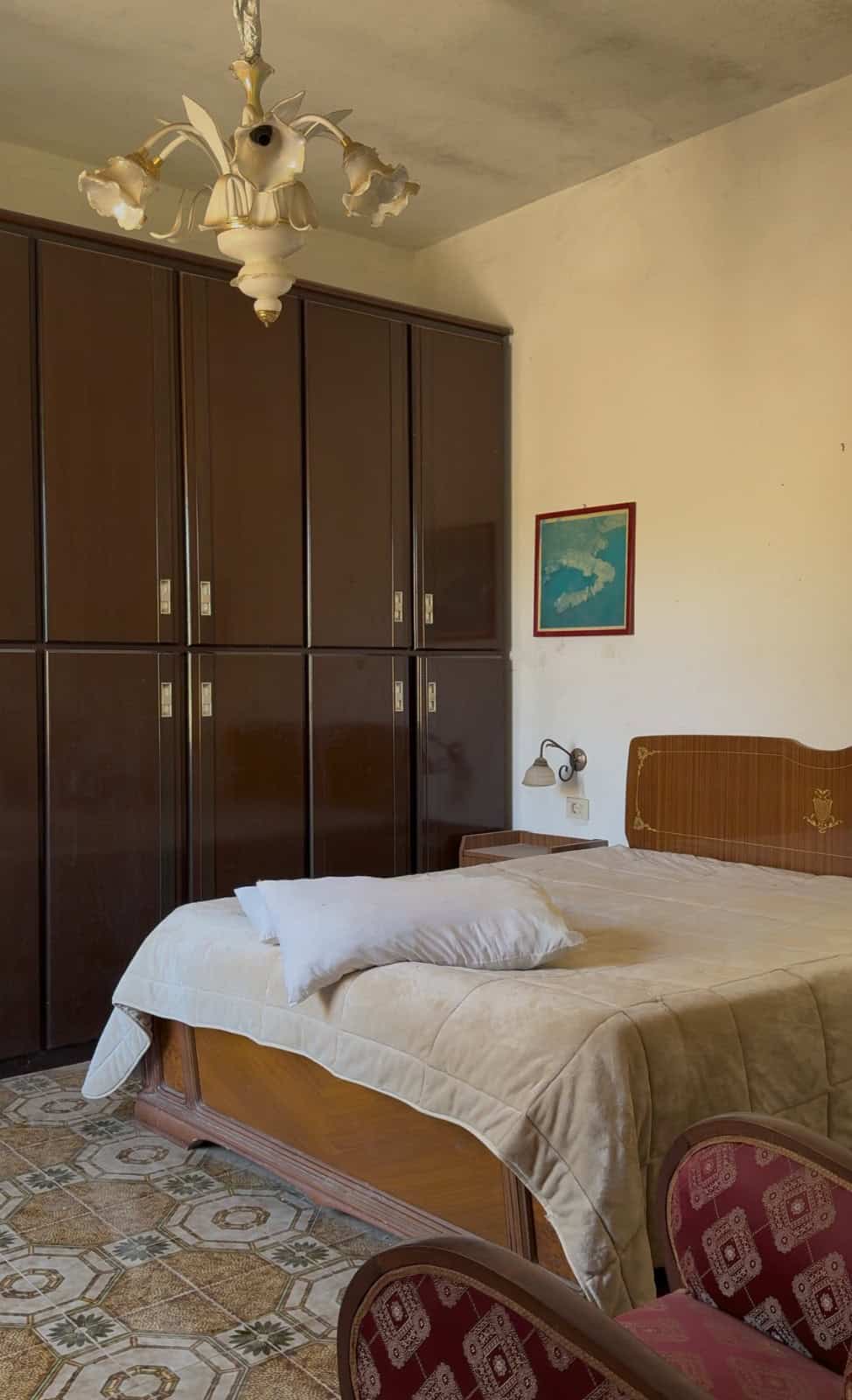 Camera da letto con armadio a muro in legno scuro, letto matrimoniale e decorazioni vintage, ambiente accogliente e luminoso.