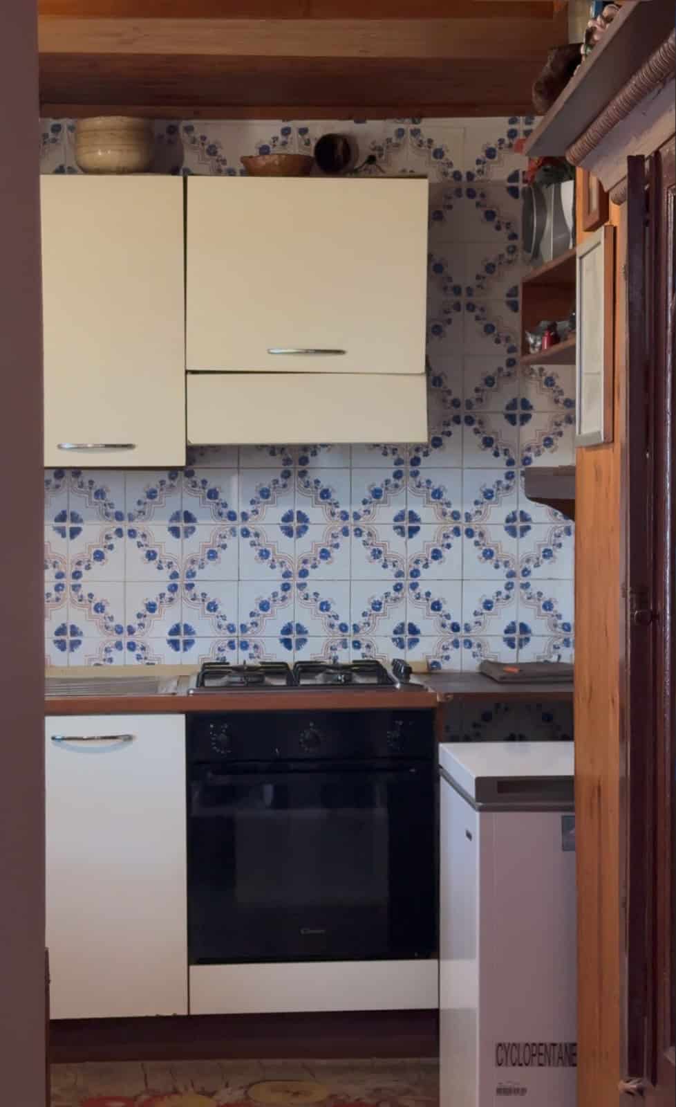 Cucina compatta con mobili bianchi, forno e parete rivestita di piastrelle blu e bianche a motivi geometrici.