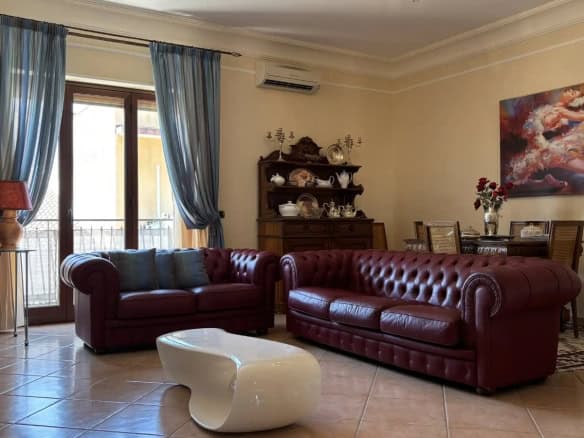 Interno di un soggiorno con divani in pelle rosso, grande finestra con tende blu e decorazioni eleganti.