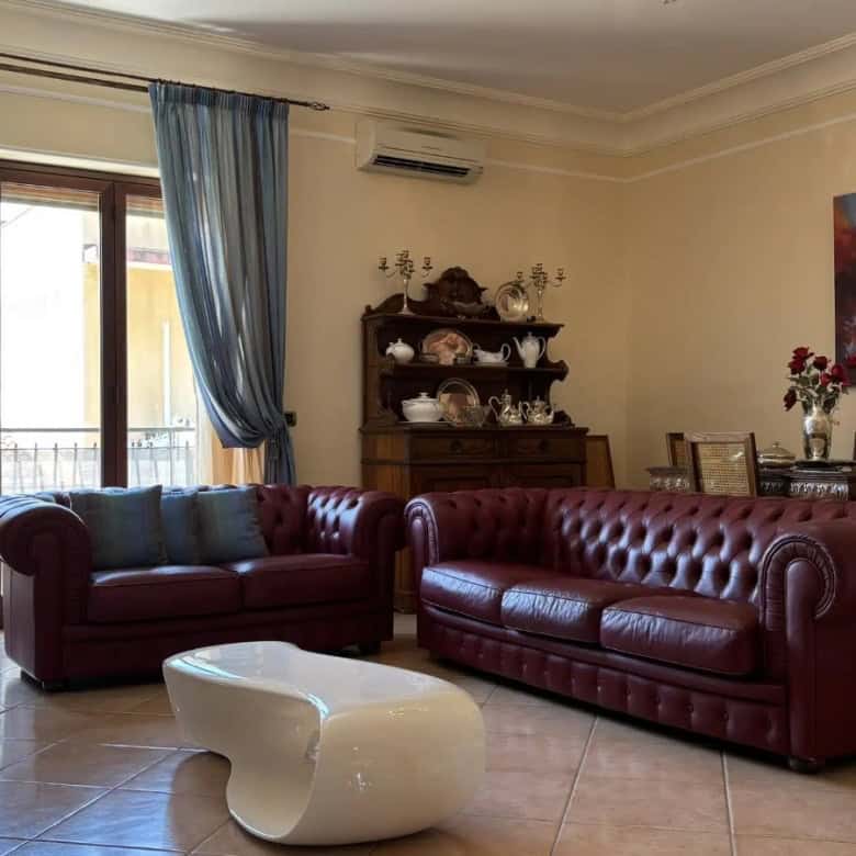 Interno di un soggiorno con divani in pelle rosso, grande finestra con tende blu e decorazioni eleganti.