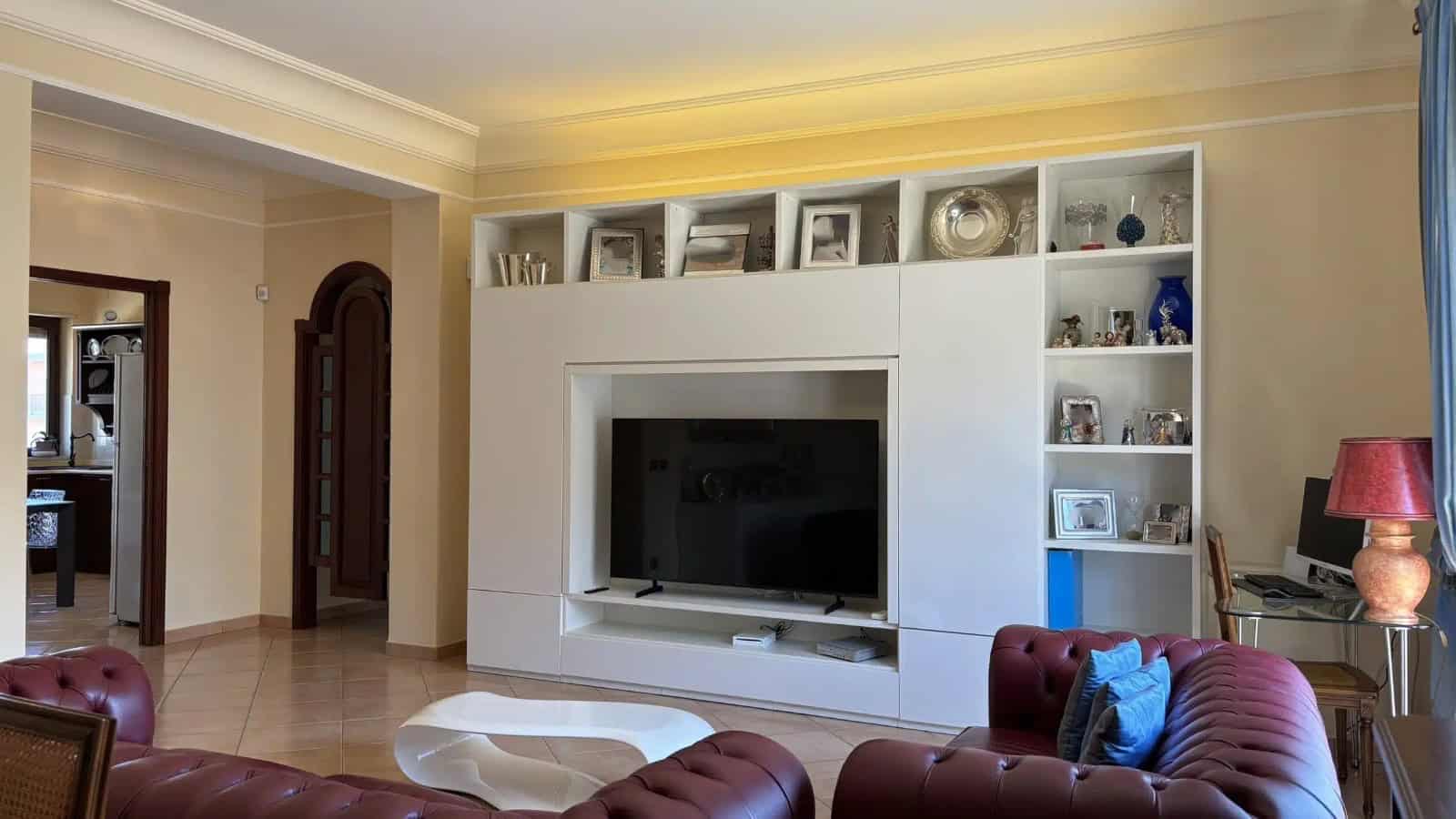Interno di un appartamento con soggiorno arredato, TV e libreria moderna, ambiente luminoso e accogliente.