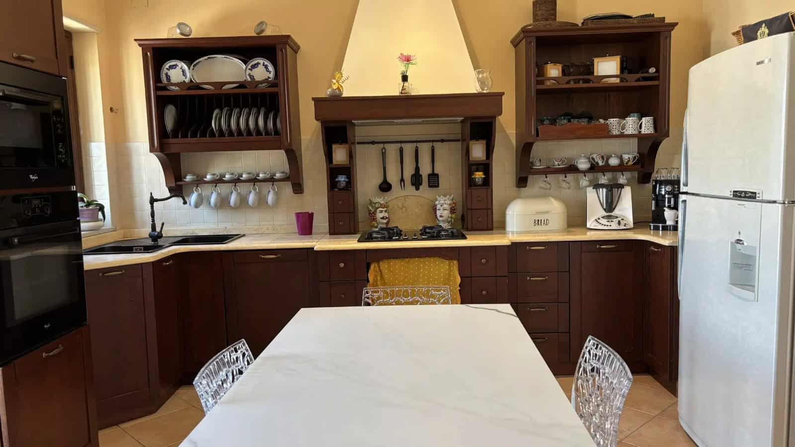 Cucina spaziosa con mobili in legno scuro, piano in marmo bianco e elettrodomestici moderni, ideale per la vendita di appartamenti a Milazzo.