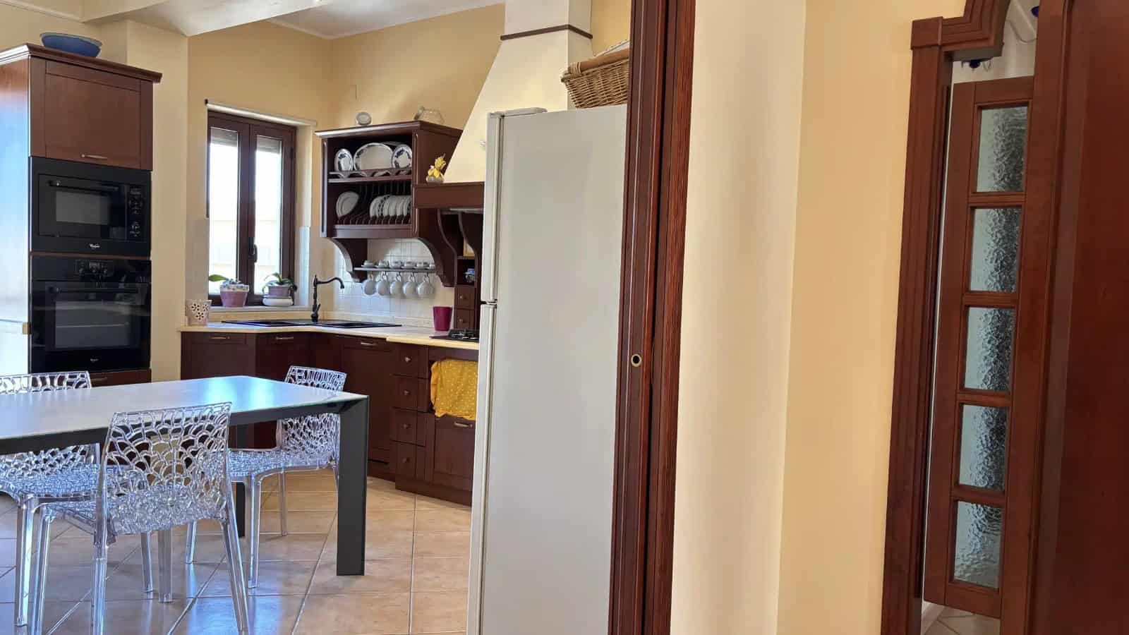 Interno di un appartamento con cucina moderna e zona pranzo, finestra luminosa e arredi in legno.