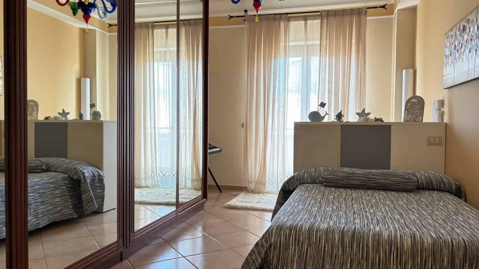 Camera da letto luminosa con grandi finestre e armadio a specchio, arredamento semplice e funzionale.