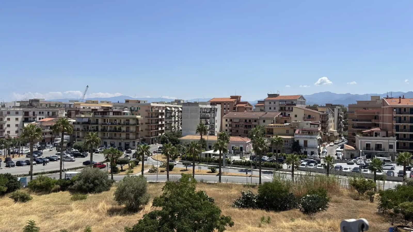 Vista panoramica di Milazzo con edifici residenziali e montagne sullo sfondo, cielo sereno.
