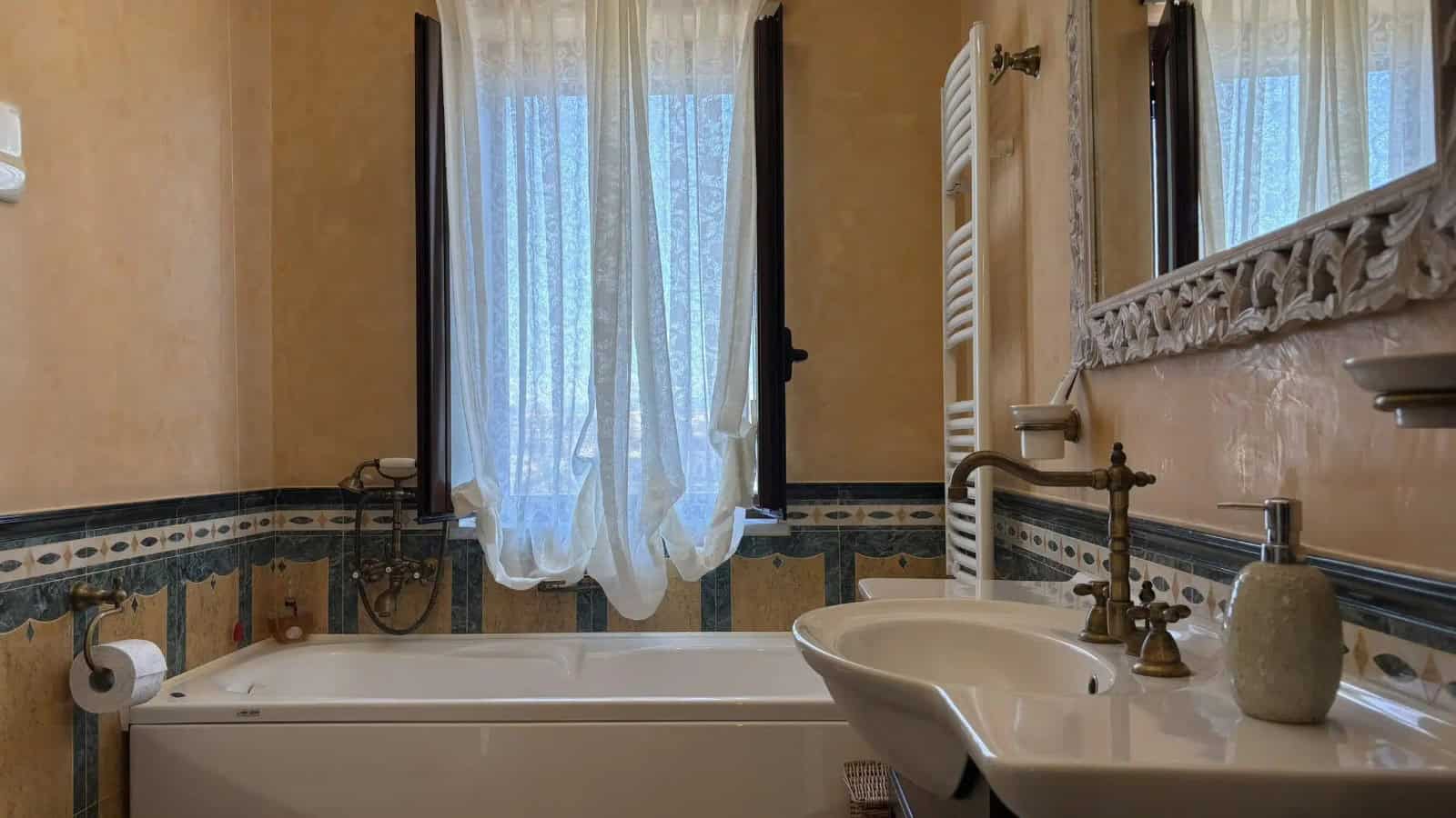 Bagno con vasca, lavabo e finestra con tende leggere in appartamento a Milazzo.