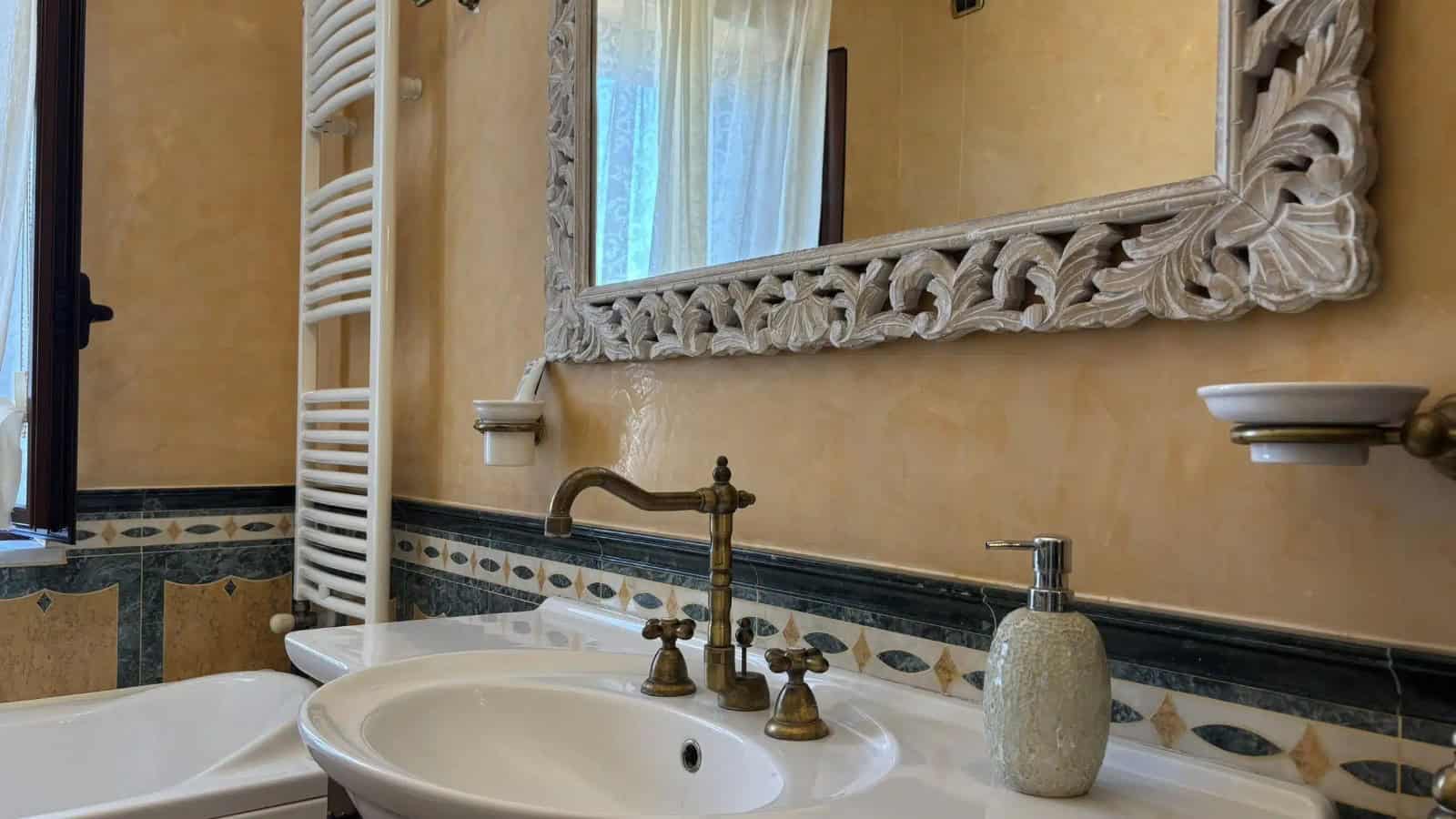 Bagno con lavabo, specchio decorato e dettagli in ottone, ambiente elegante e luminoso.