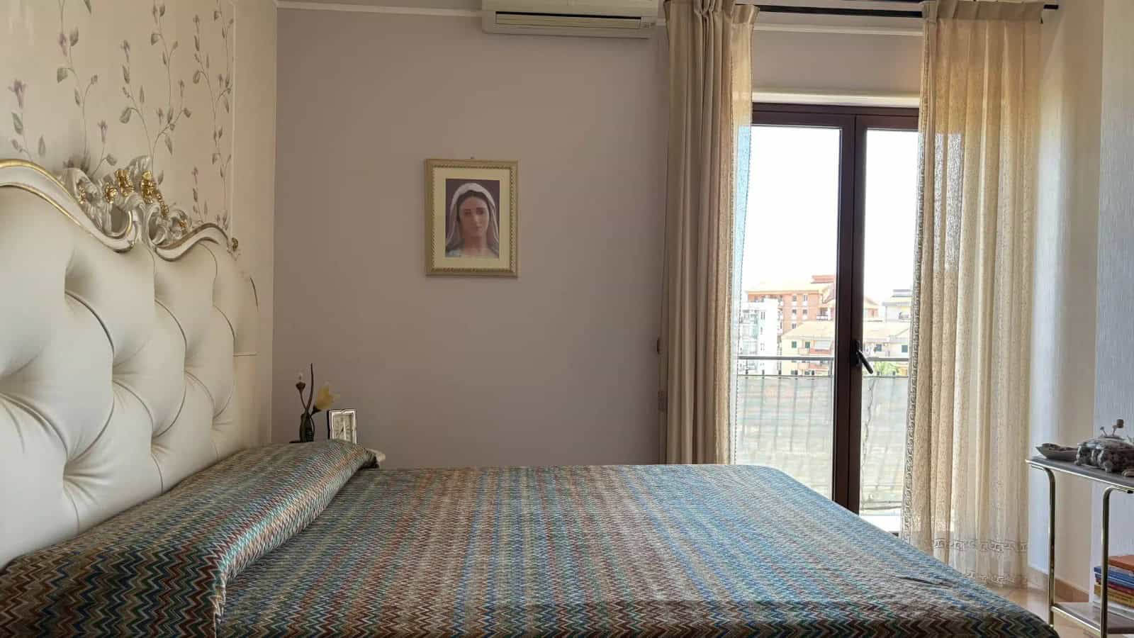 Camera da letto luminosa con letto matrimoniale, pareti decorate e vista su balcone con tende leggere.