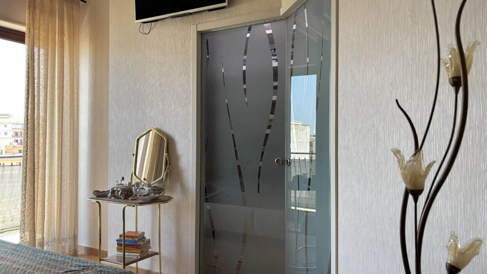 Interno di un appartamento con porta in vetro decorata, specchio e arredi eleganti, vista sulla città.