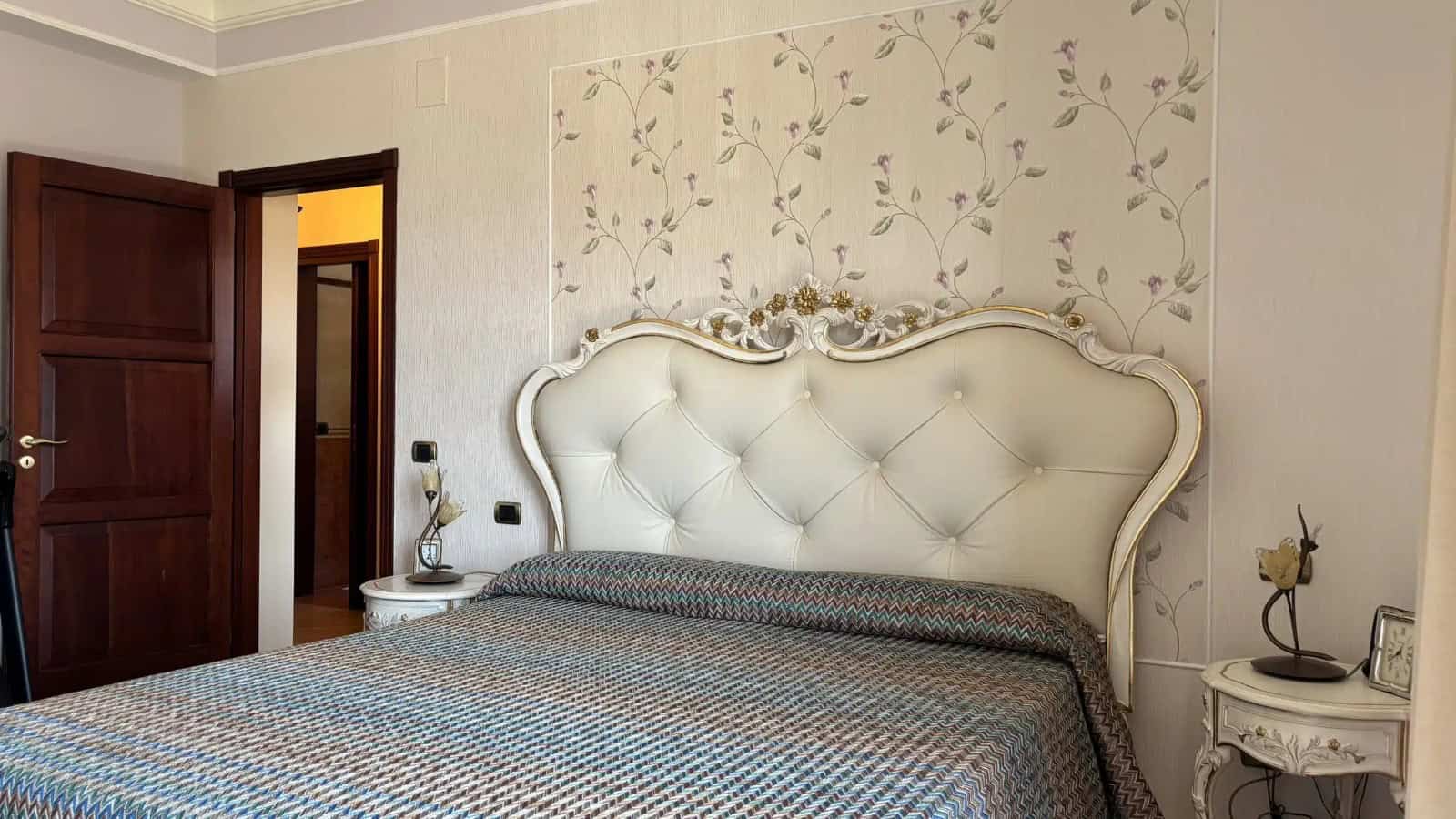 Camera che mostra una camera da letto elegante con testiera imbottita e decorazioni floreali sulla parete.