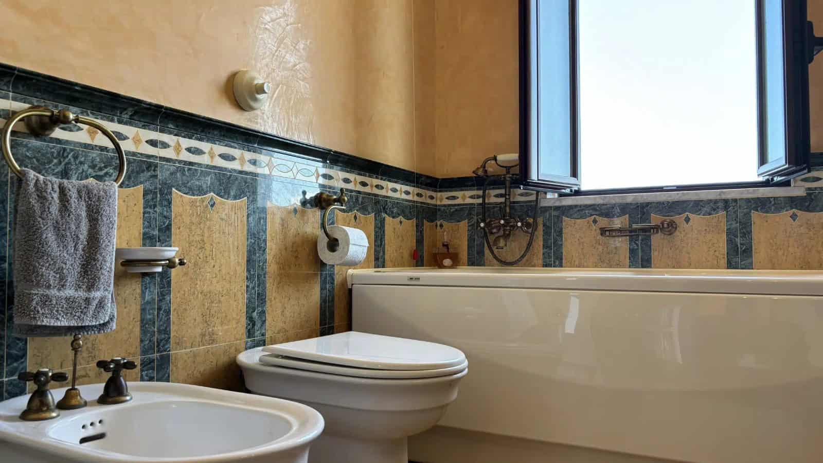 Bagno con vasca, lavabo e WC in un appartamento a Milazzo, vista sulla finestra.