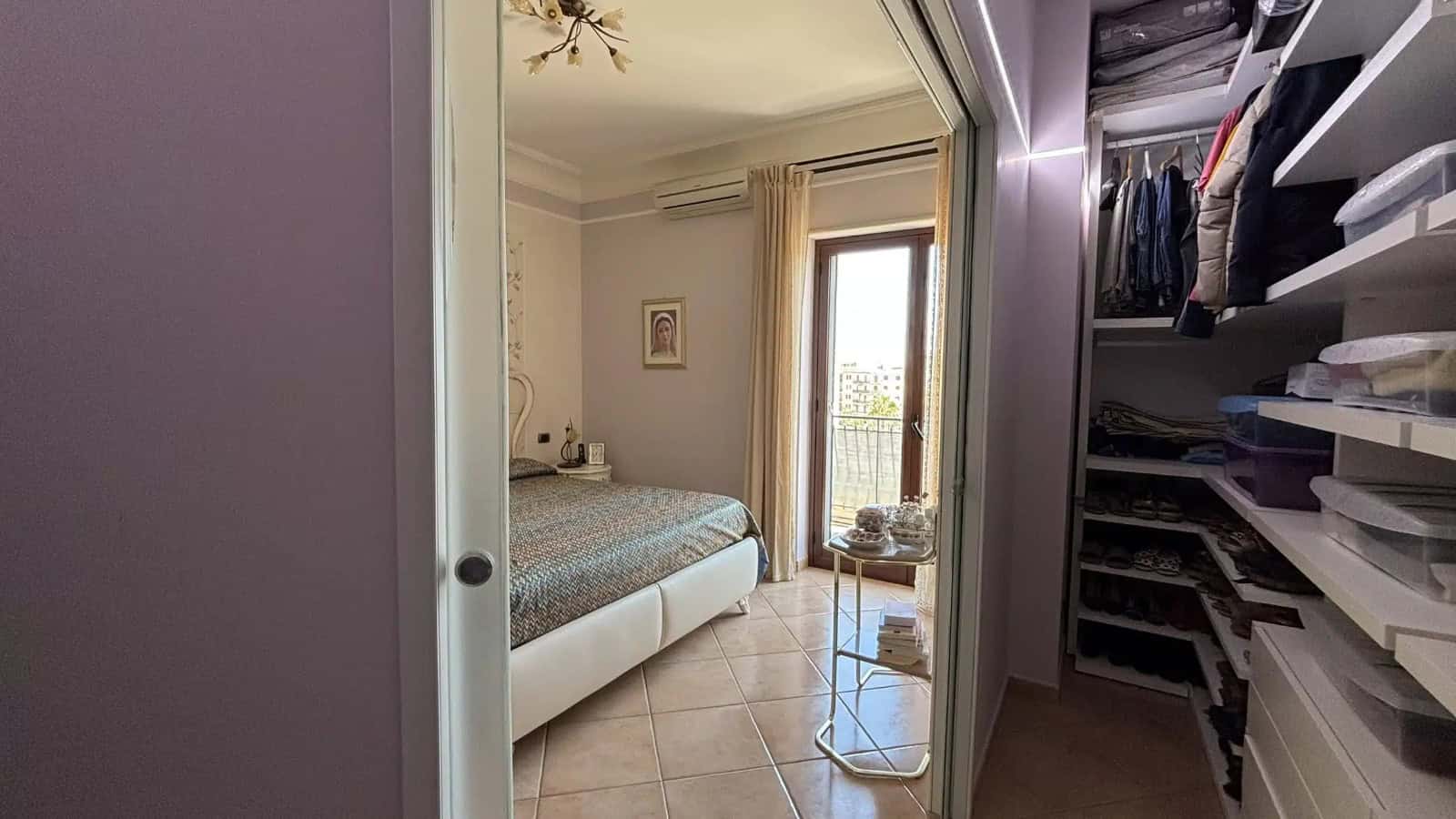 Camera che mostra una camera da letto moderna con letto matrimoniale, armadio a muro e accesso a un balcone con vista panoramica.