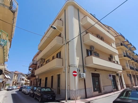 Edificio residenziale in vendita in Via Luigi Pirandello a Capo d'Orlando, con balconi e negozi al piano terra, sotto un cielo azzurro.