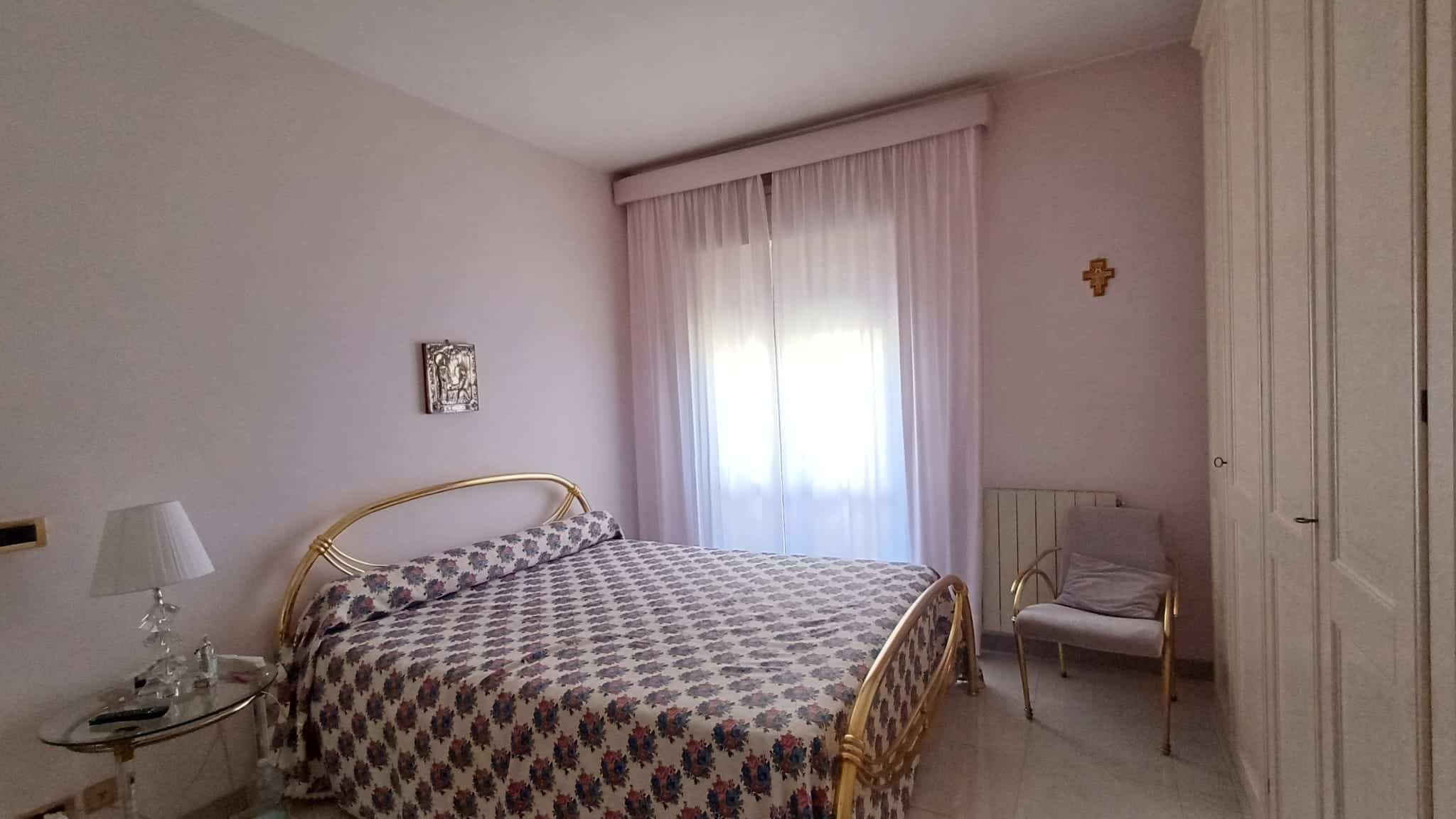 Camera da letto luminosa con letto matrimoniale, tende leggere e arredi eleganti in stile classico.