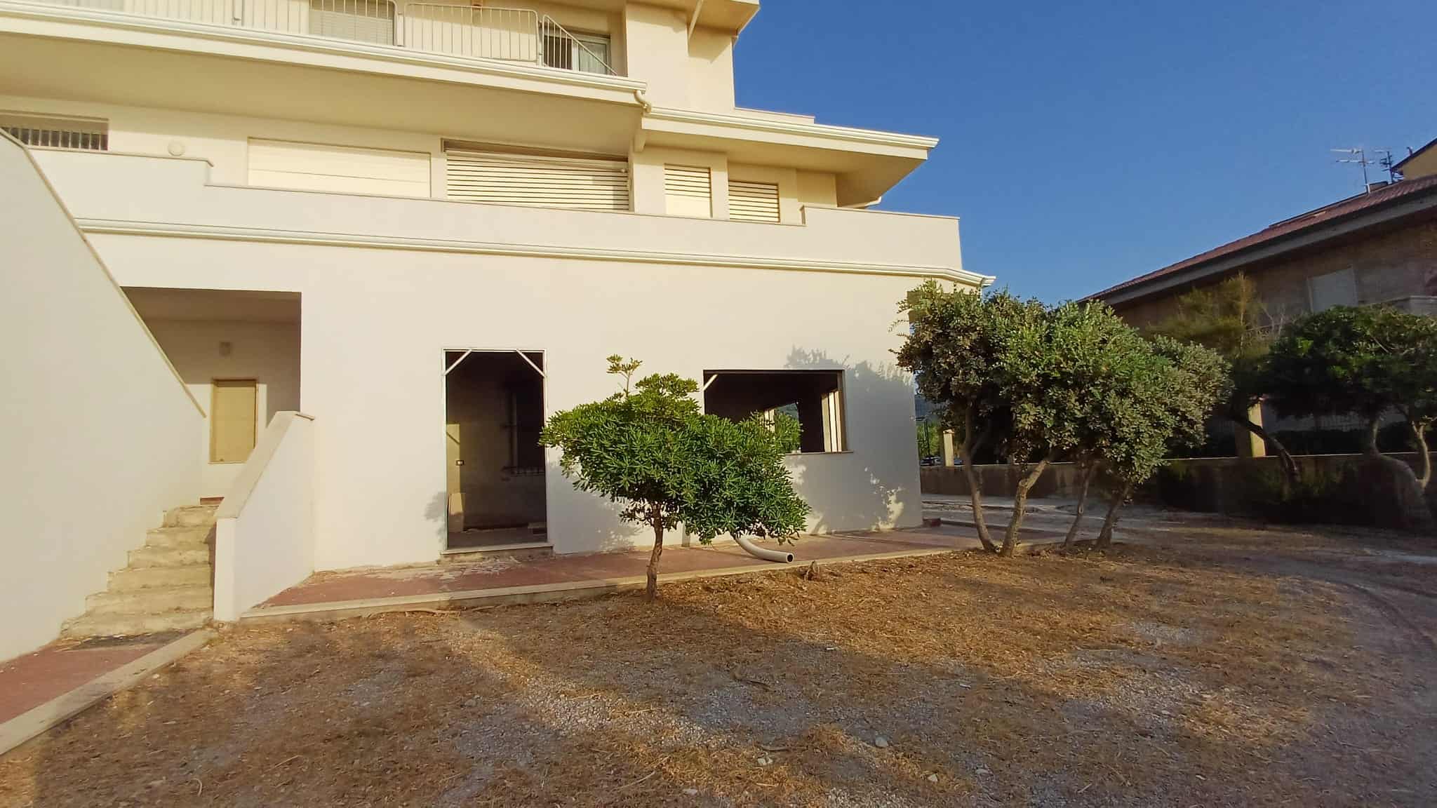Facciata di un edificio commerciale a Capo d'Orlando con ingresso e giardino con alberi.