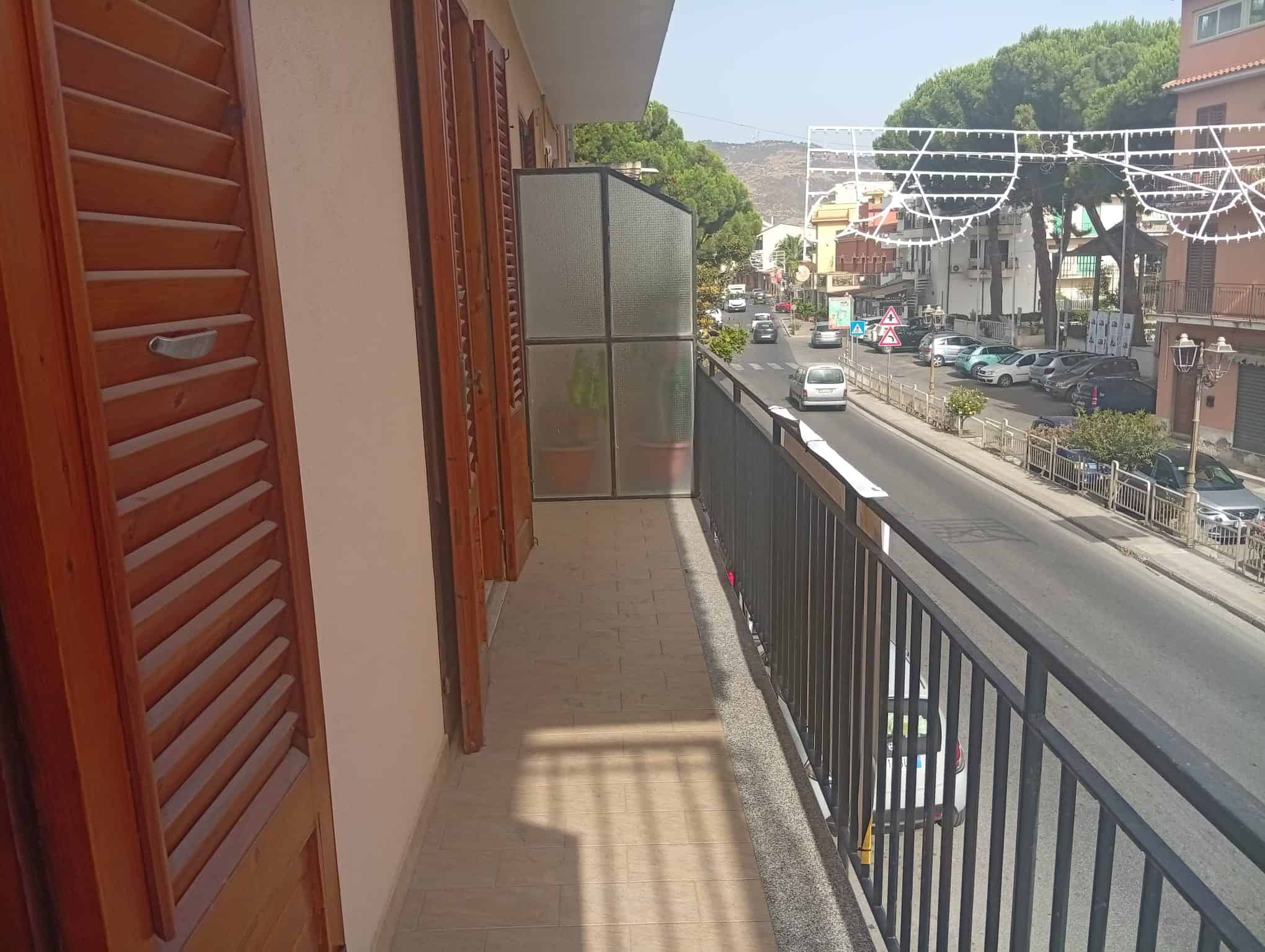 Balcone di un appartamento con vista sulla strada principale di Falcone, con decorazioni luminose e edifici circostanti.