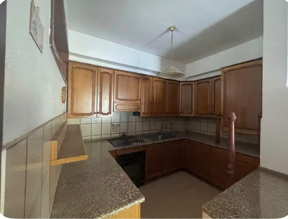 Cucina abitabile con mobili in legno e piano in granito, illuminata da luce naturale e lampada a soffitto.