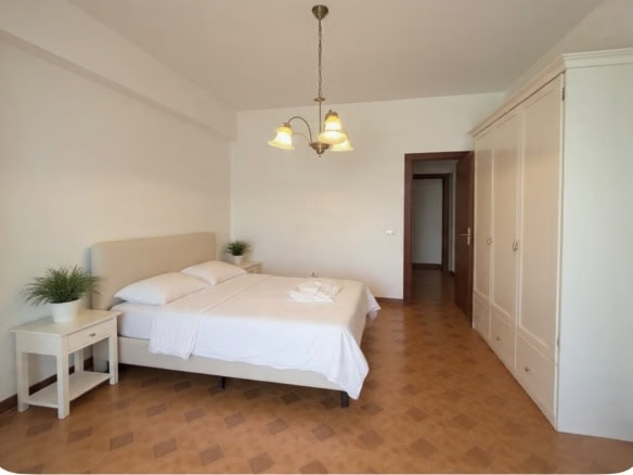 Camera da letto luminosa con letto matrimoniale, armadio grande e lampadario a soffitto in stile classico.