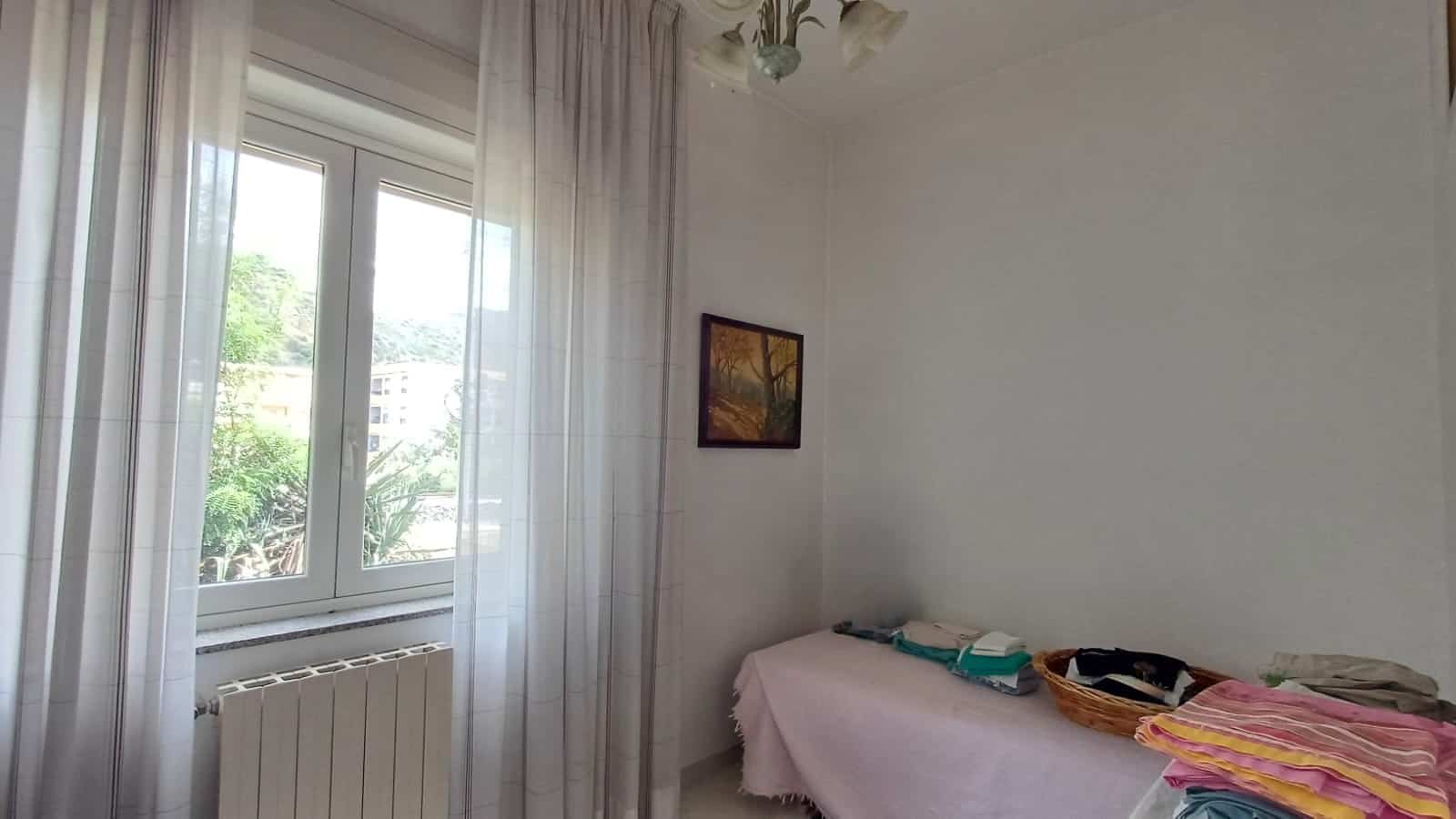 Camera da letto luminosa con finestra grande, tende leggere e arredi semplici, ideale per un appartamento in vendita a Capo d'Orlando.