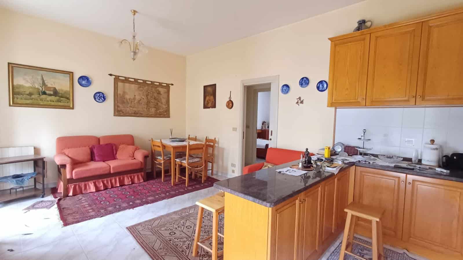 Interno di un appartamento in vendita a Capo d'Orlando, con soggiorno e cucina aperta, mobili in legno e decorazioni colorate alle pareti.