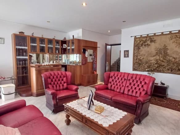 Salotto spazioso con divani rossi, parete con arazzo e mobile in legno con vetrine, ambiente luminoso e accogliente.