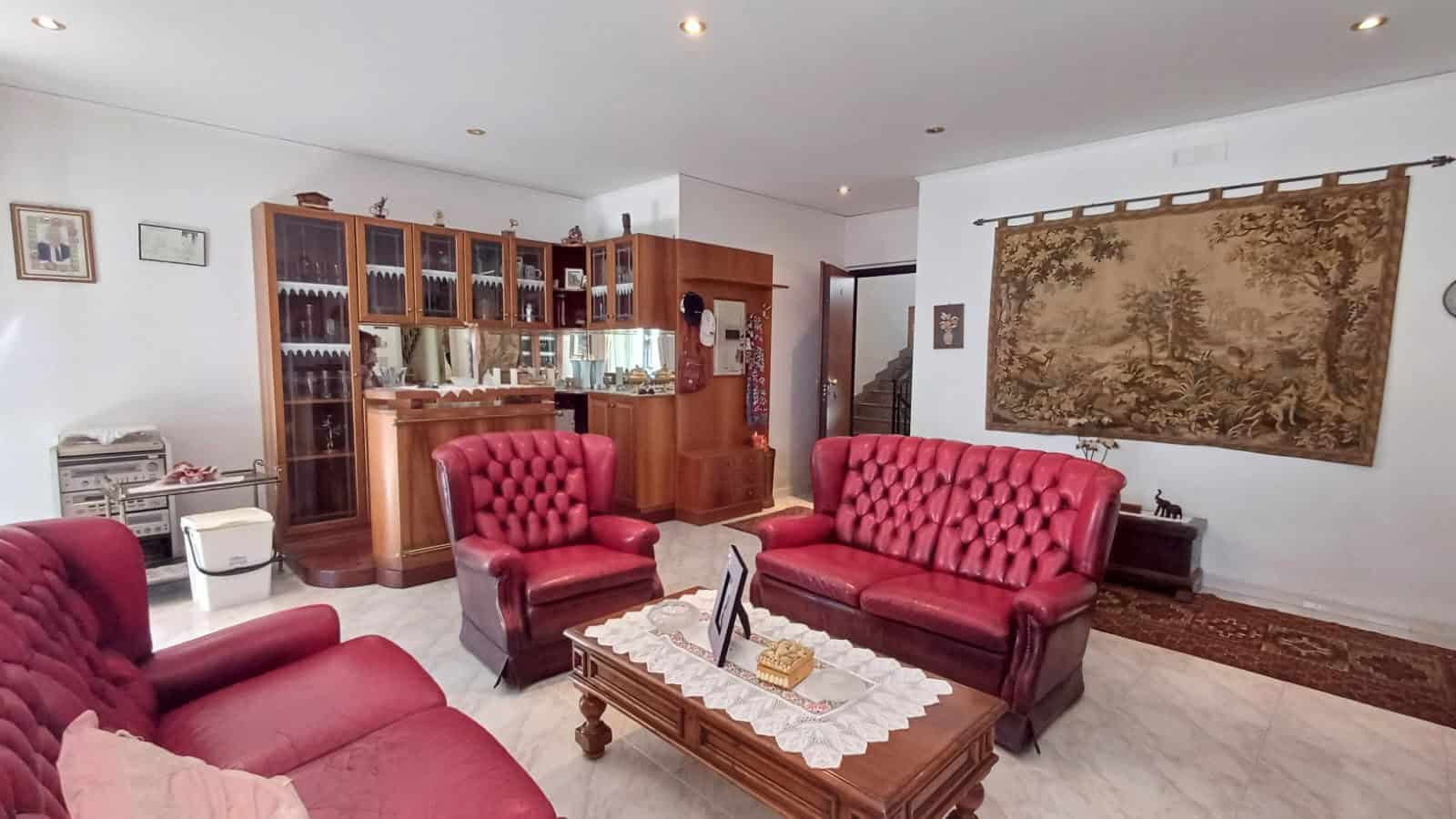 Salotto spazioso con divani rossi, parete con arazzo e mobile in legno con vetrine, ambiente luminoso e accogliente.