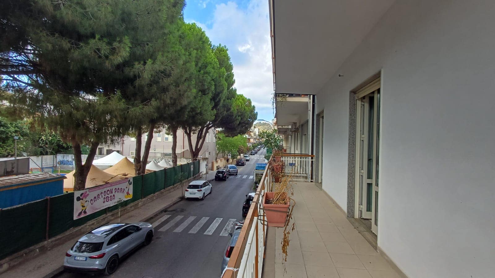 Balcone di un appartamento con vista sulla strada e alberi, in zona residenziale di Capo d'Orlando.