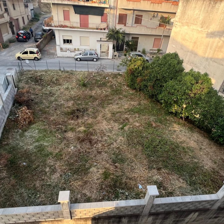 Spazio esterno di un cortile condominiale con prato e arbusti, vista dall'alto in un quartiere residenziale.