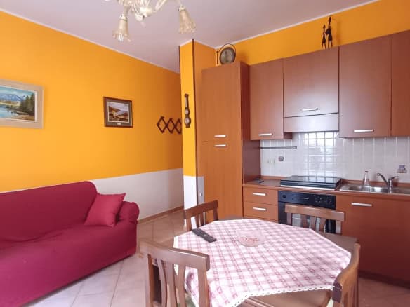 Interno di un appartamento con pareti arancioni, divano rosso e cucina in stile semplice con mobili in legno e pareti rivestite di piastrelle.