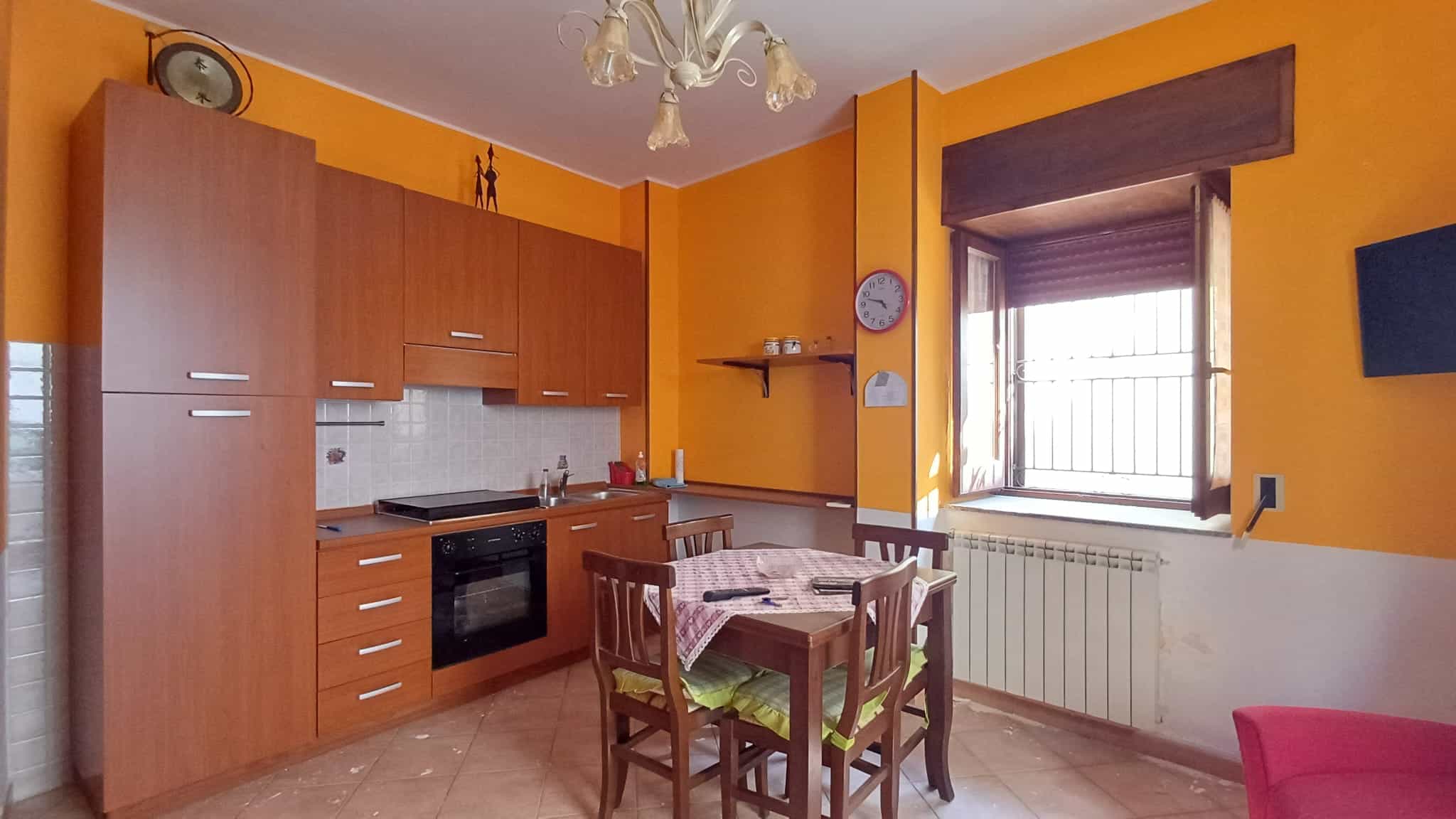 Interno di un appartamento con cucina e zona pranzo, pareti arancioni e mobili in legno chiaro.