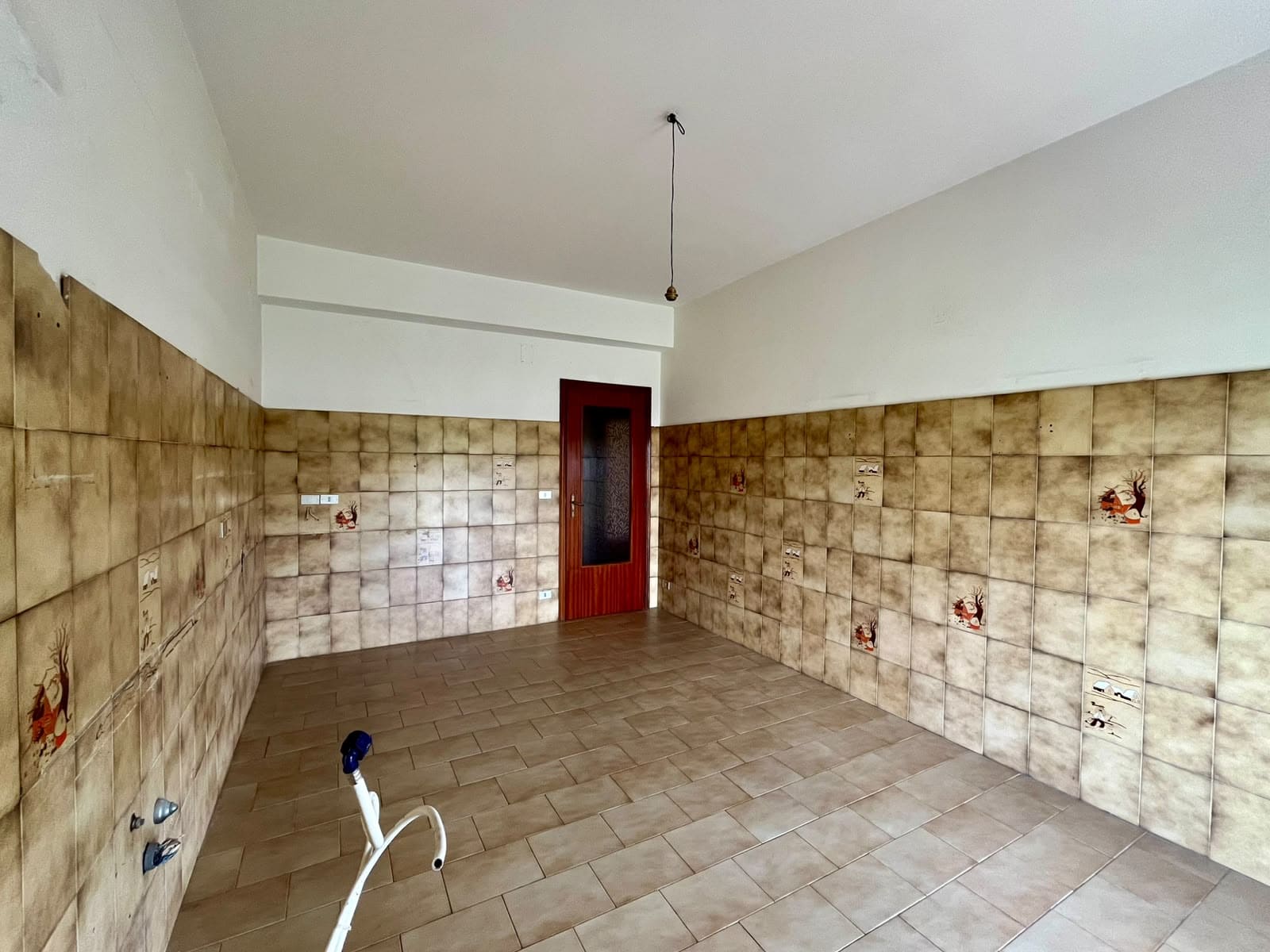 Interno di un appartamento in vendita in via Don Silvio Cucinotta, Pace del Mela, con pareti rivestite in piastrelle beige e porta in legno.