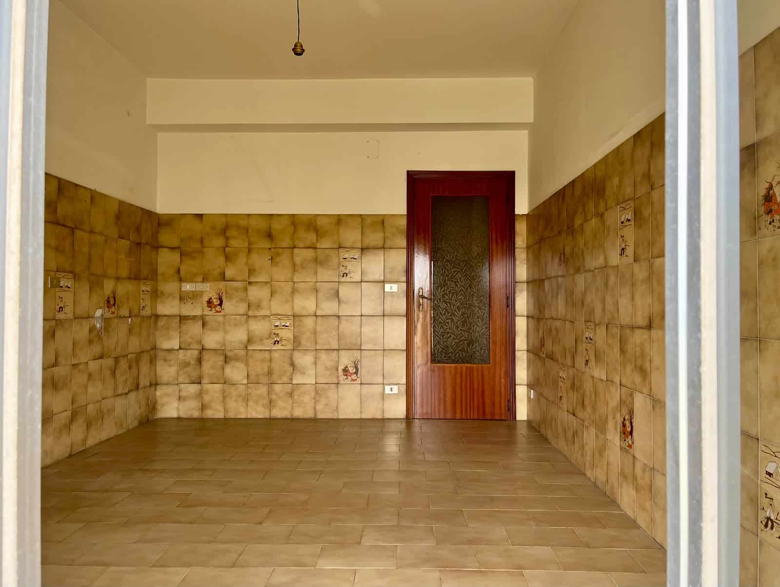 Stanza vuota in appartamento in vendita a Pace del Mela con pareti rivestite di piastrelle beige e porta in legno.