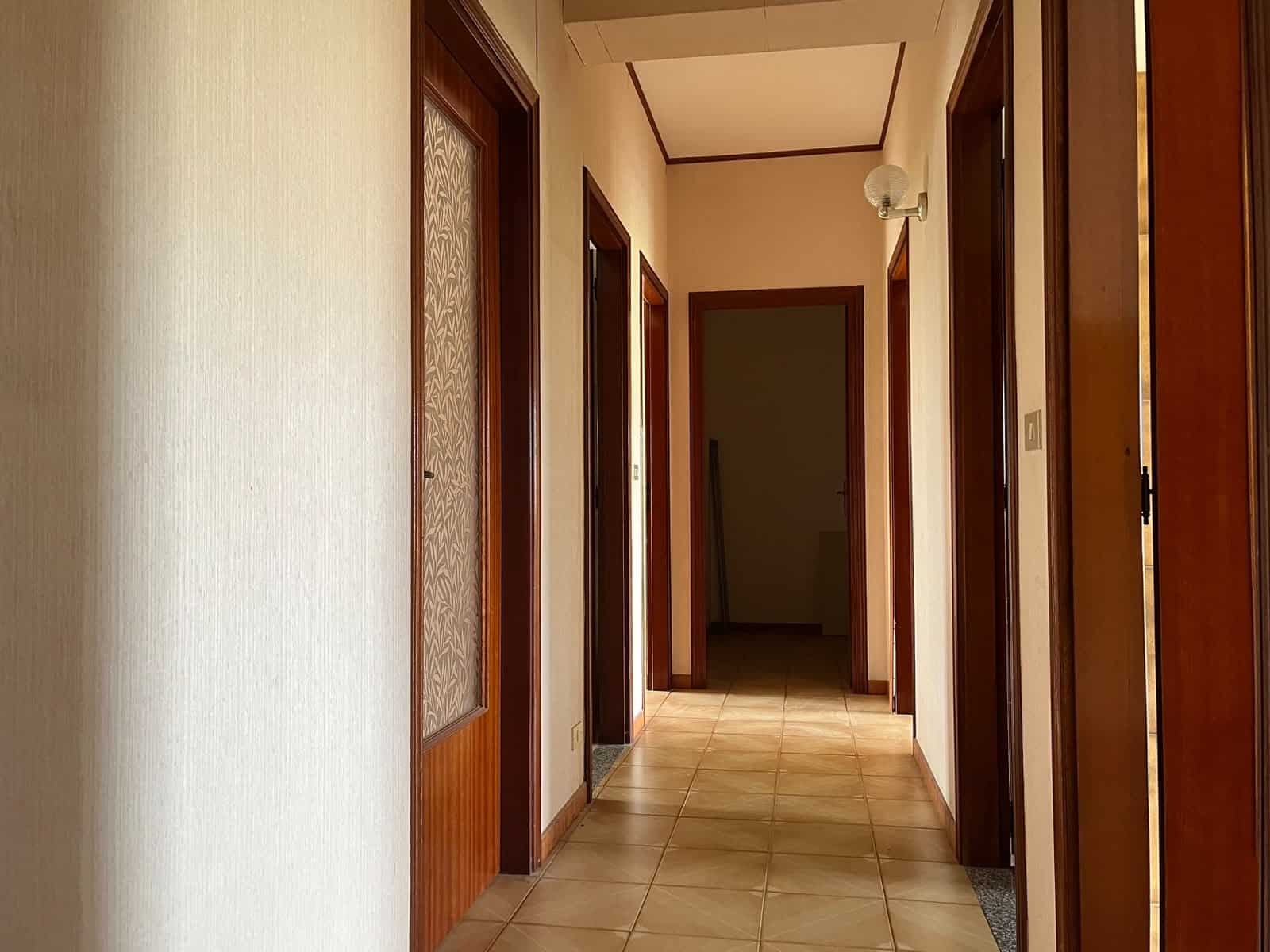 Interno di un appartamento in vendita a Pace del Mela, vista corridoio con porte in legno e pareti chiare.