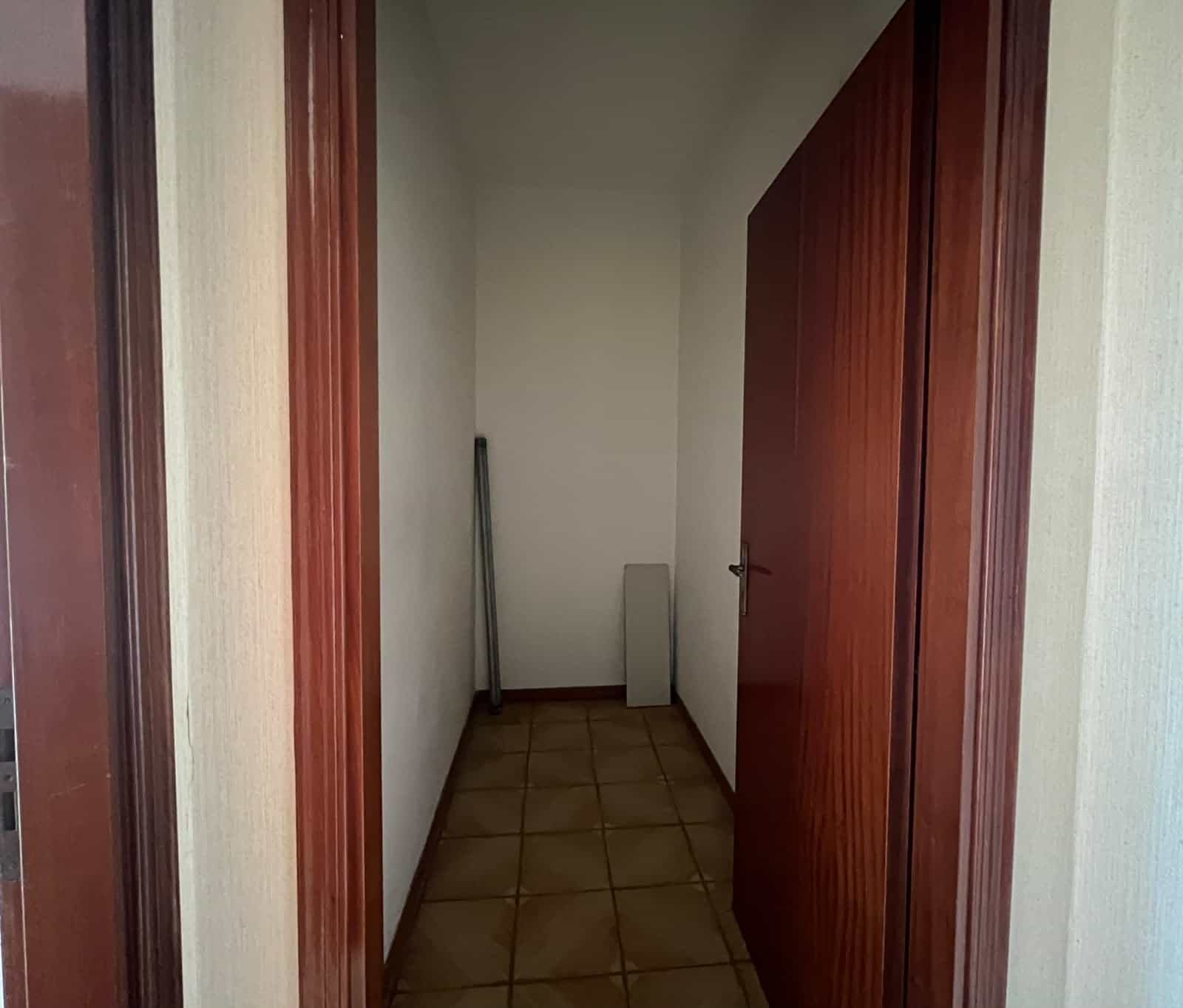 Ingresso di un appartamento con porta in legno e pavimento in piastrelle beige.