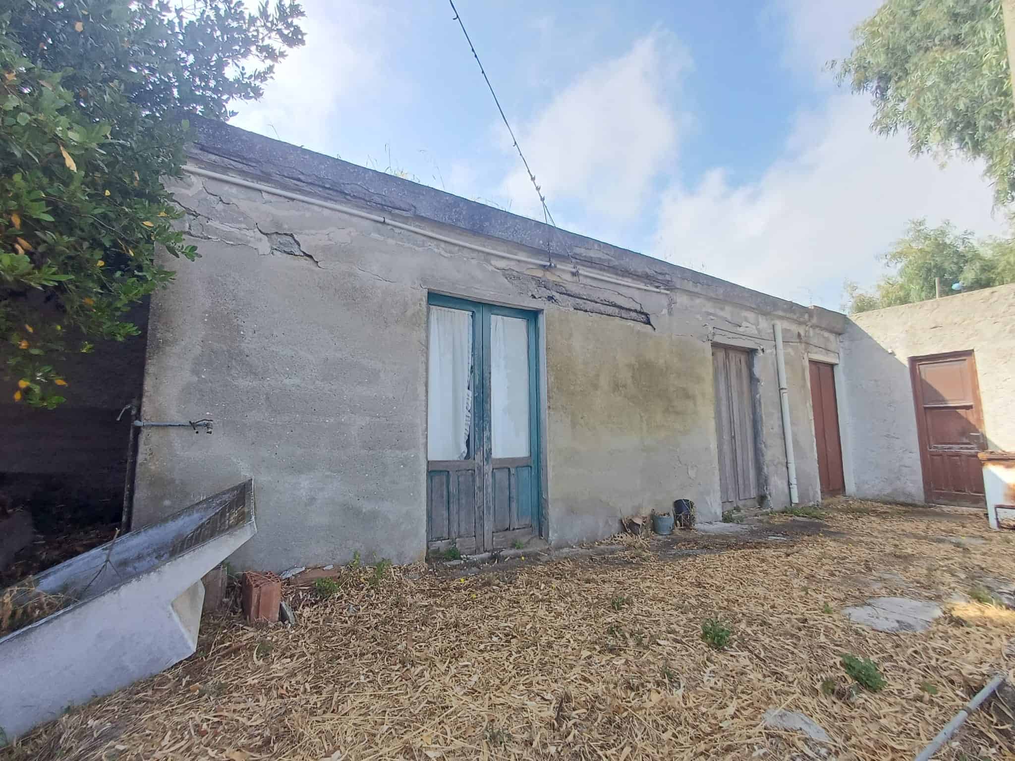 Casa in vendita a Capo d'Orlando, struttura rustica con pareti in cemento e porte in legno, immersa nel verde.