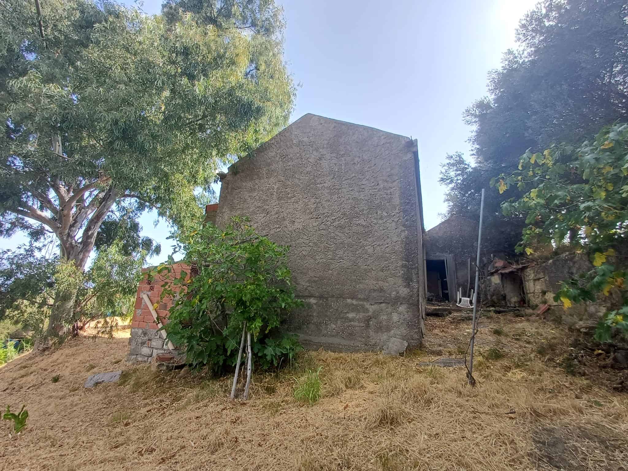 Edificio in costruzione o ristrutturazione in zona collinare con alberi e vegetazione circostante.