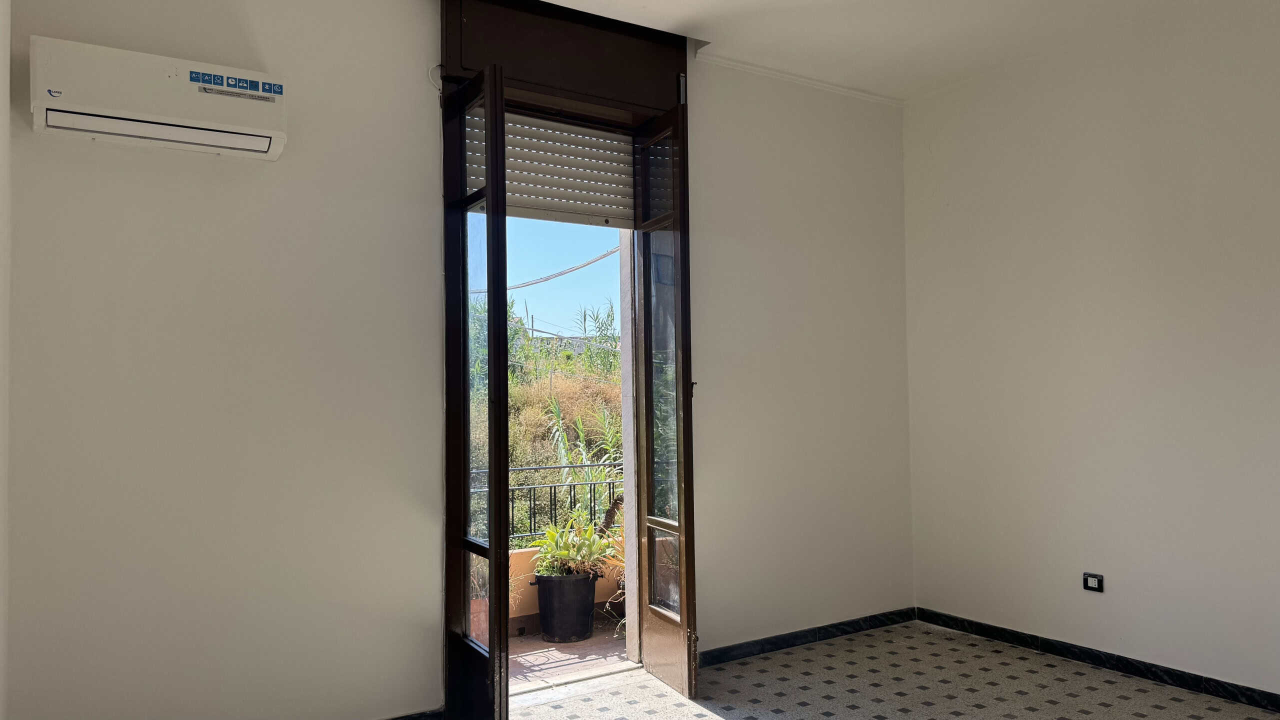 Interno di una casa semindipendente con porta finestra che dà su un balcone, pareti bianche e pavimento in piastrelle nere e bianche.