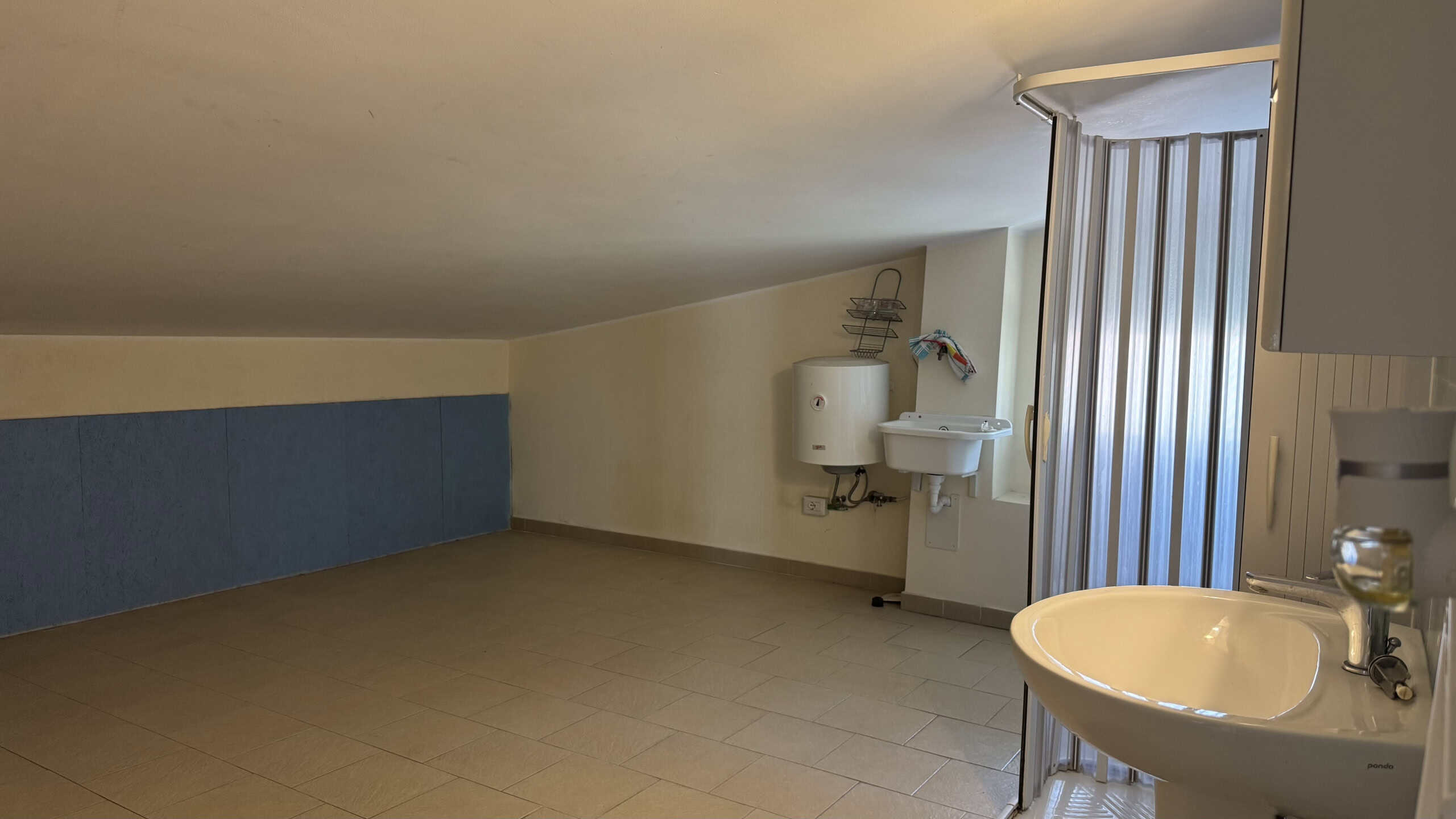Spazio vuoto in un appartamento in affitto a Milazzo, con pareti bianche, pavimento in piastrelle e una porta finestra che dà su un balcone.