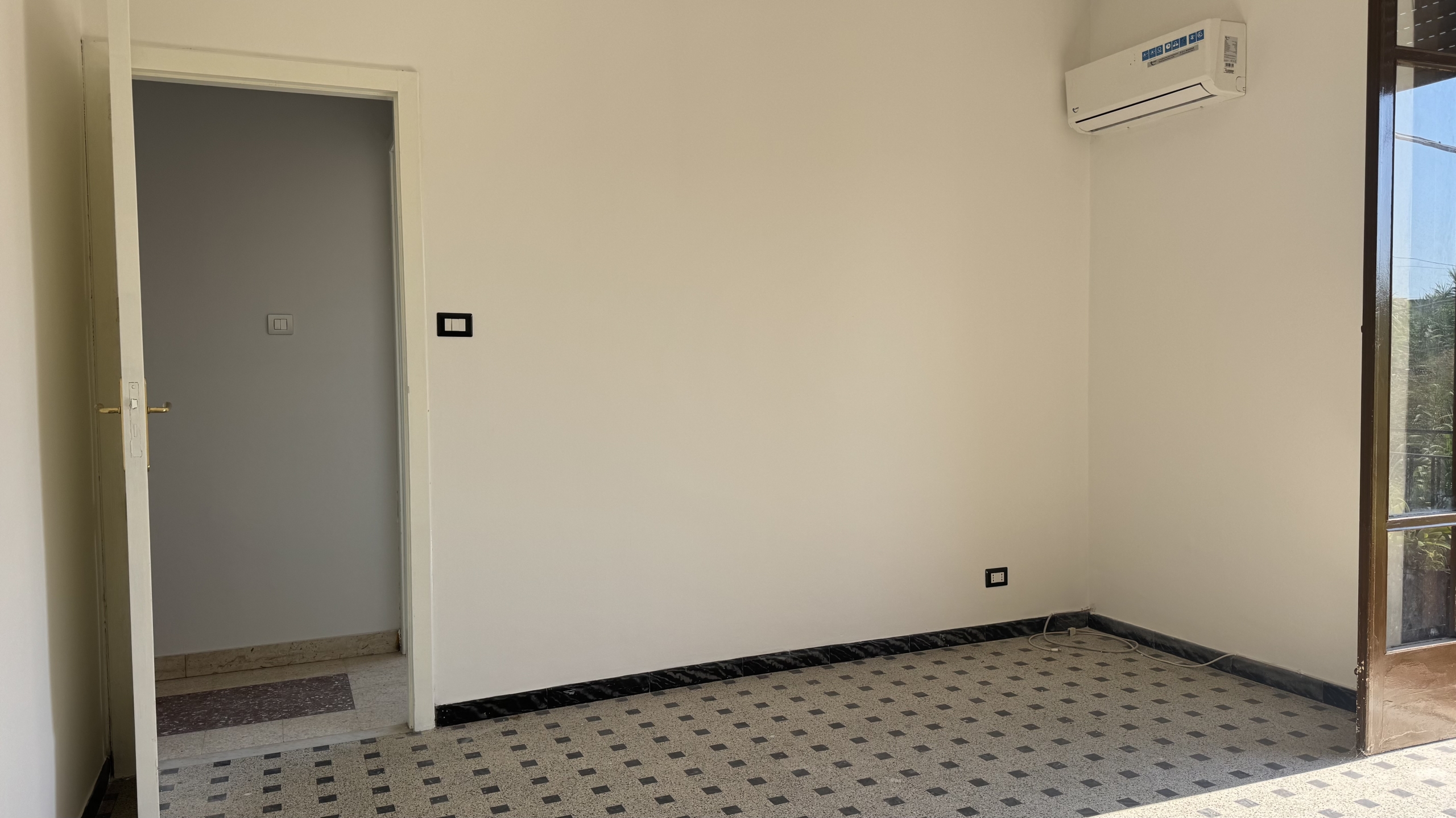 Interno di una stanza vuota con aria condizionata e porta verso un balcone, ideale per una casa in vendita a Venetico.