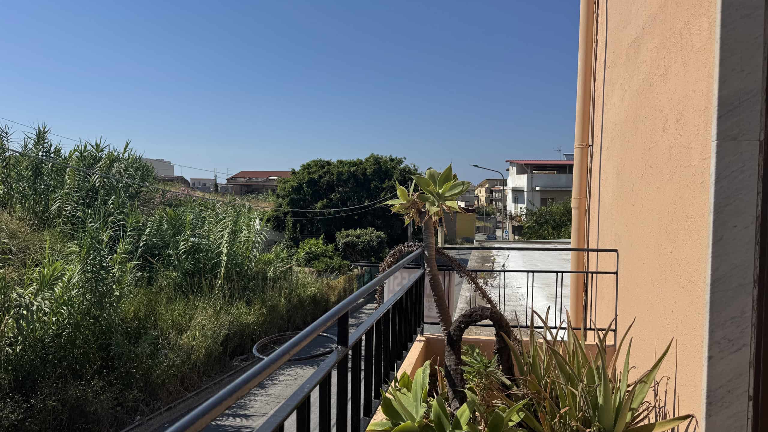 Balcone con vista su giardino e case a Venetico, Sicilia, in una giornata soleggiata.