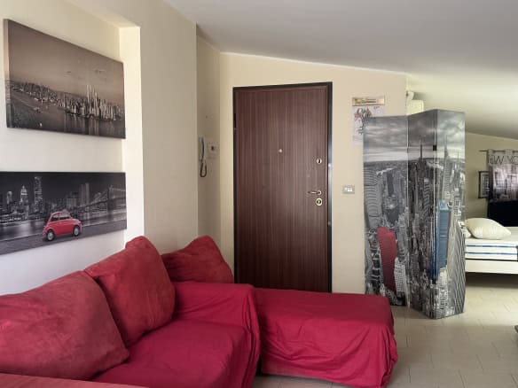 Interno di un appartamento in affitto a Milazzo, con divano rosso e pareti decorate con foto di città.